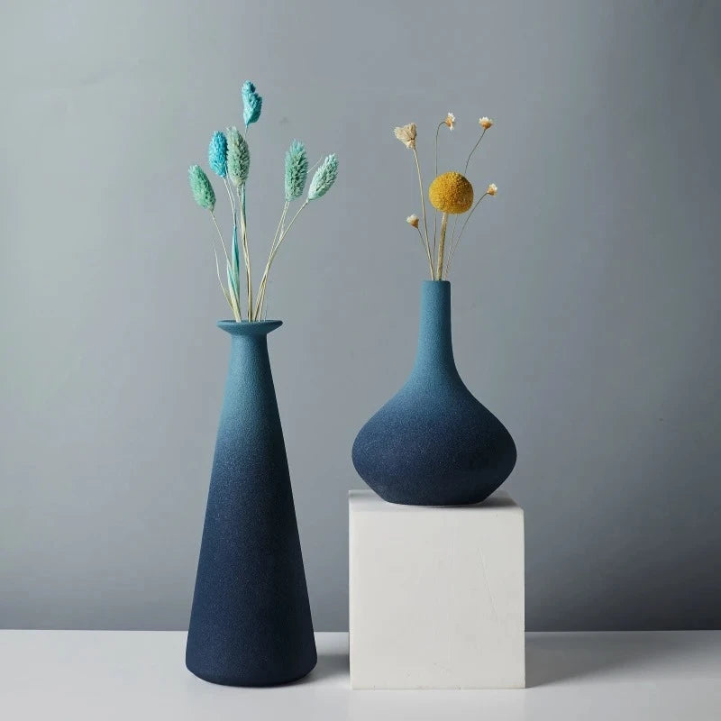 Two Blue Ceramic Vases on a white square with flowers inside 