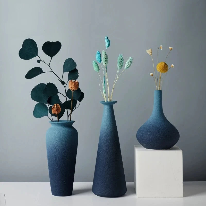 Three Blue Ceramic Vases with flowers inside on a white square