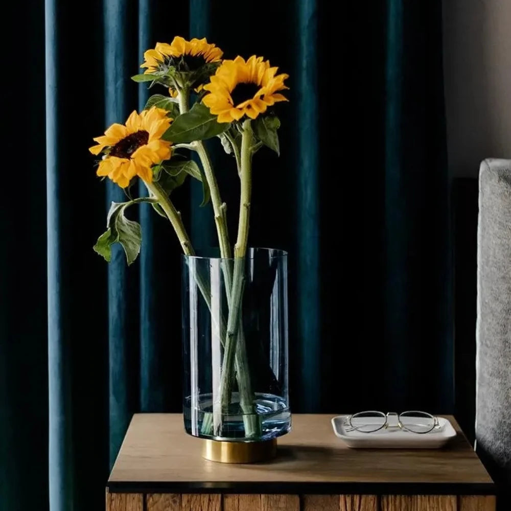 Large Blue Glass Cylinder Vase with sunflowers inside on a wooden cabinet