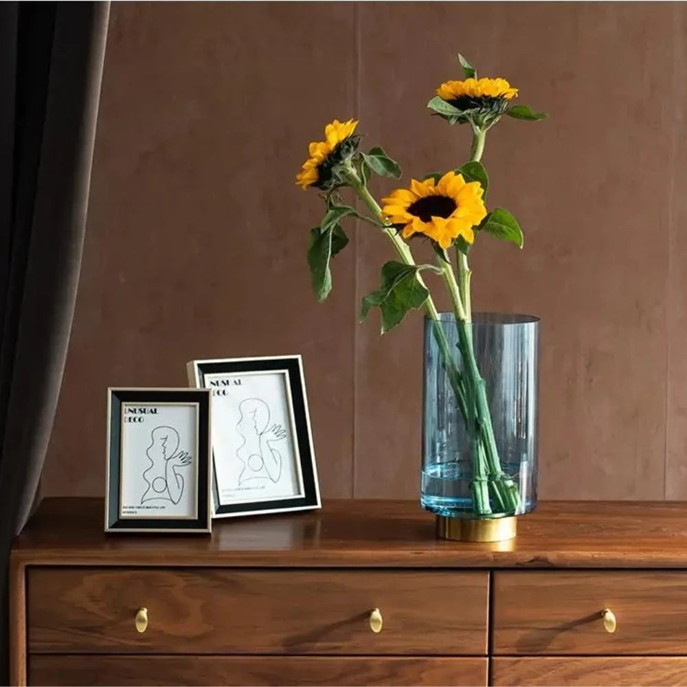 Blue Glass Cylinder Vase with sunflowers inside on a wooden dresser