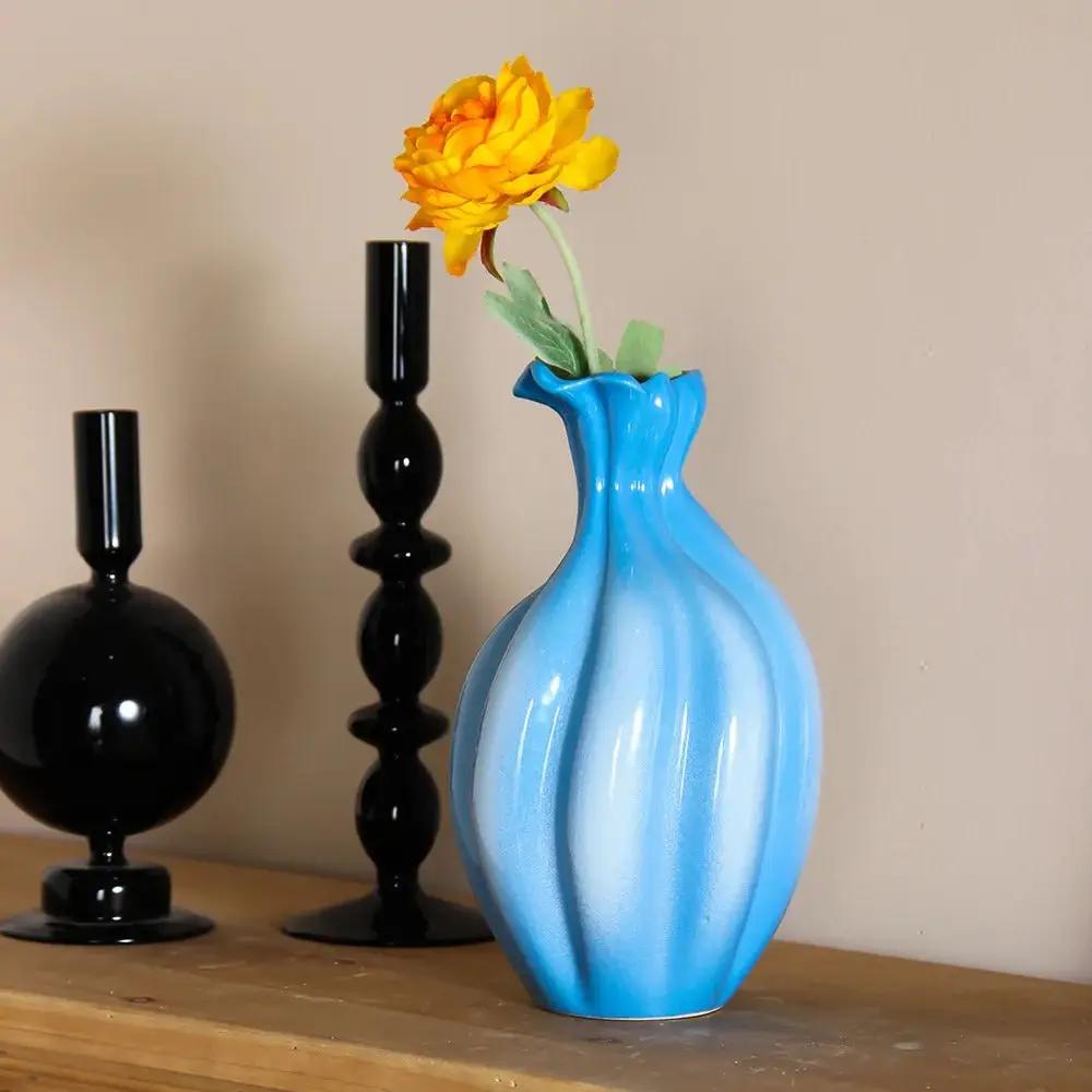 Blue and White Vase with a yellow flower inside next to black decorative elements