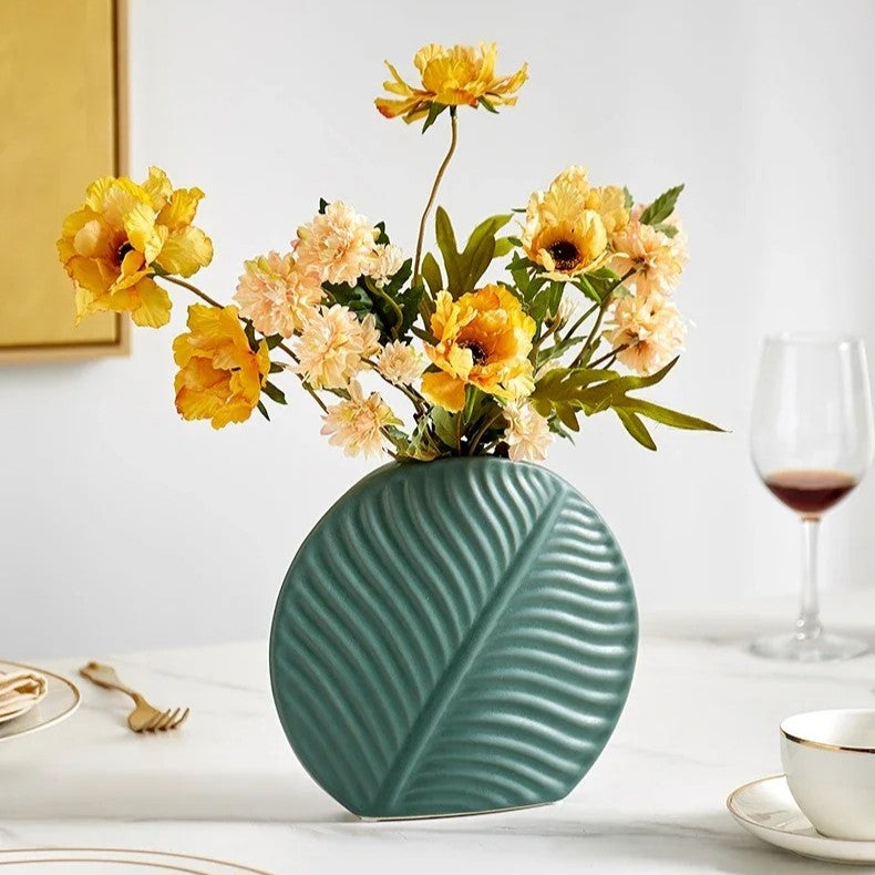 Green Boho Flower Vase with flowers inside on a white table next to a mug