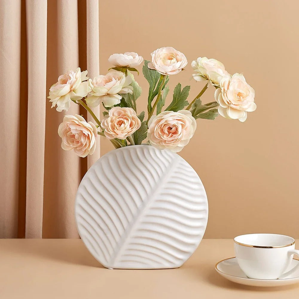 White Boho Flower Vase with flowers inside next to a cup on a peach surface