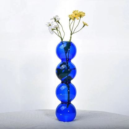 Blue Bubble Bud Vase with yellow and white flowers inside on a gray surface