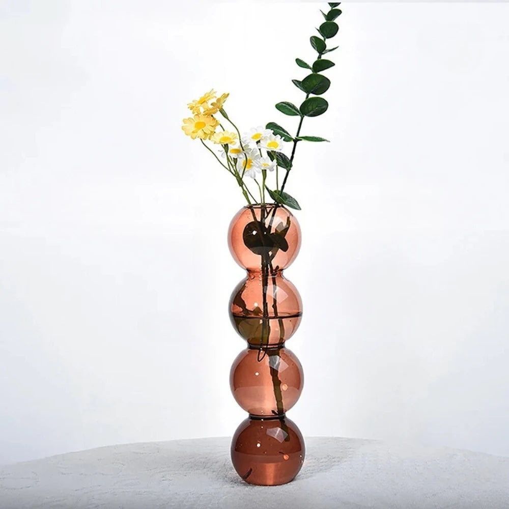 Red Bubble Bud Vase with flowers and greenery inside on a gray surface