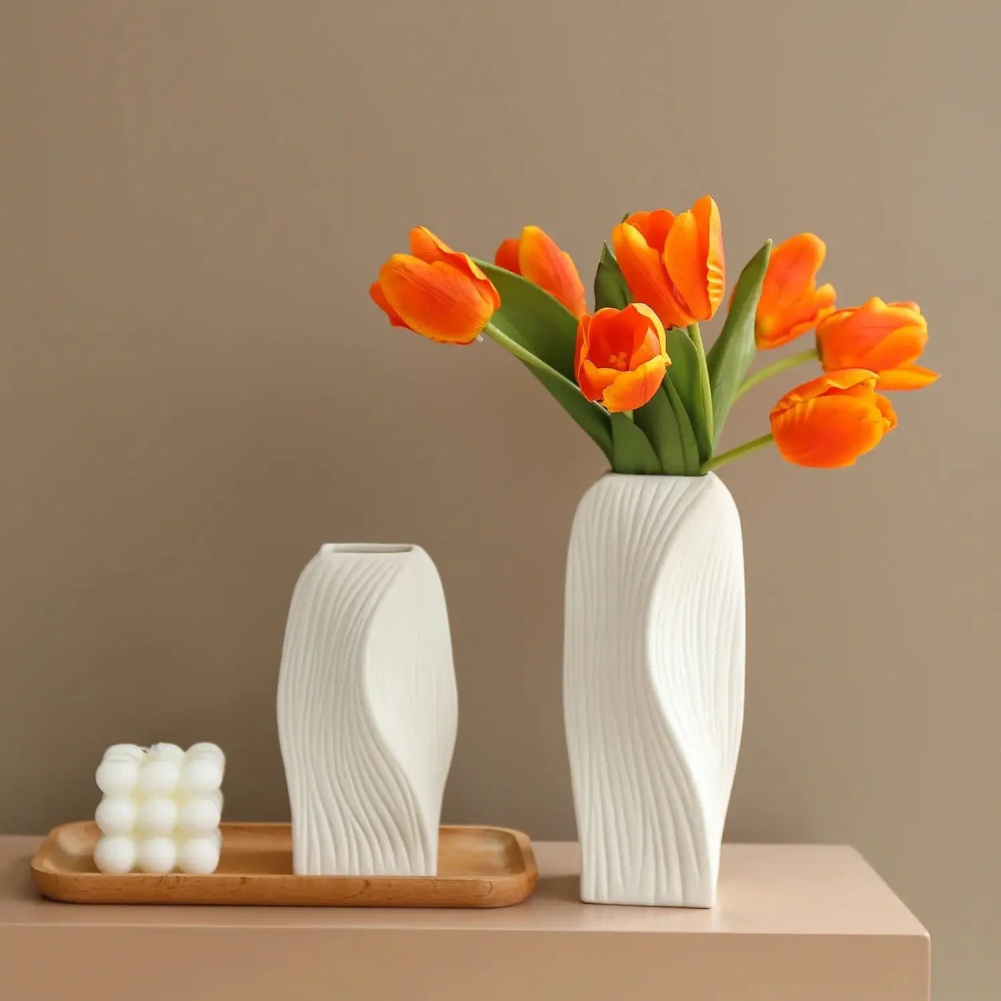 Two Ceramic Bud Vases on a brown tray next to a white candle with orange tulips inside