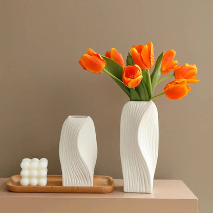 Two Ceramic Bud Vases on a brown tray next to a white candle with orange tulips inside