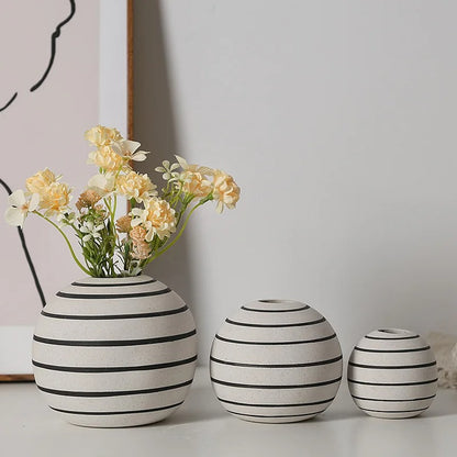 Three Ceramic Round Vases in Small, Mediun and Large with beige flowers inside in front of a gray wall with a picture