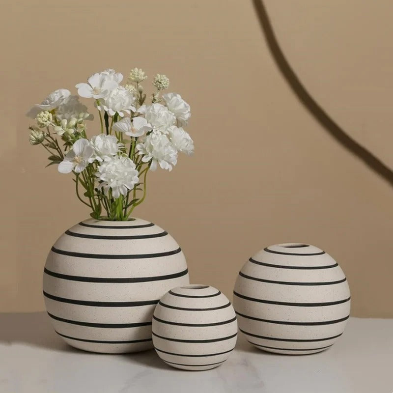 Three Ceramic Round Vases in Large, Small and Medium with white flowers inside on a grey table