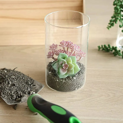 Crystal Cylinder Vase with dirt inside next to a shovel on a wooden table