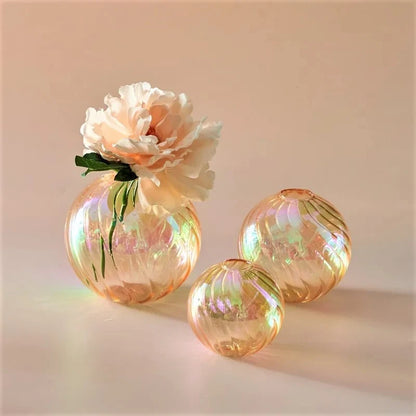 Orange Glass Round Vases with flowers inside on a peach surface