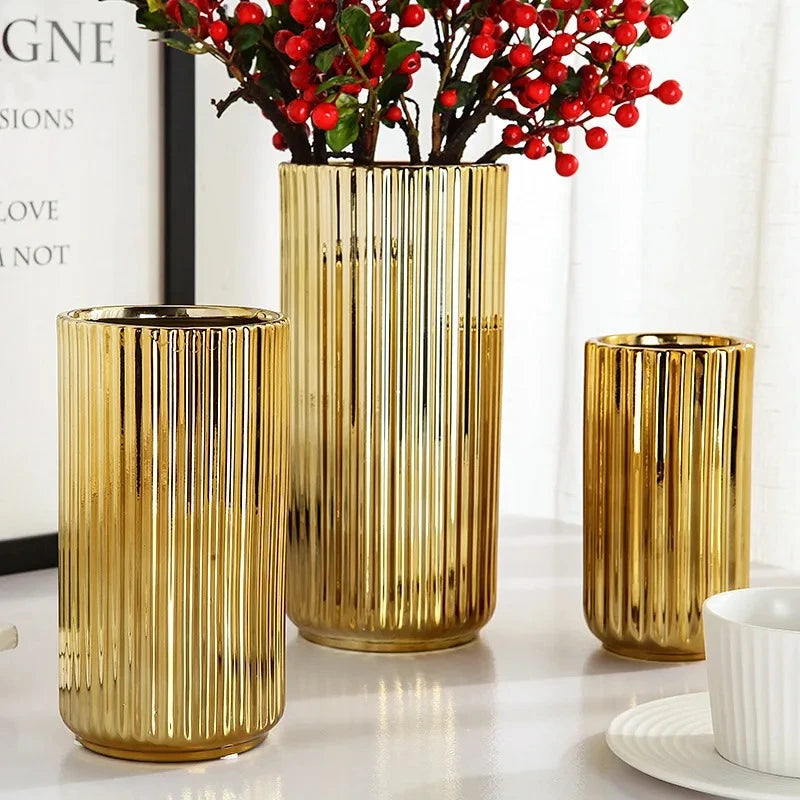 Three Cylinder Gold Vases with red flowers inside on a shiny white table