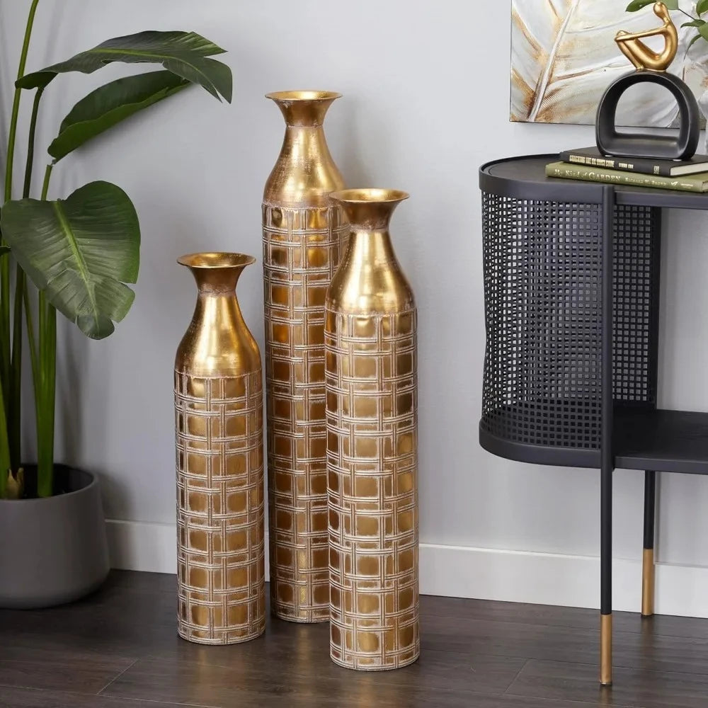 Three Gold Floor Vases on a wooden floor and next to a nightstand and greenery