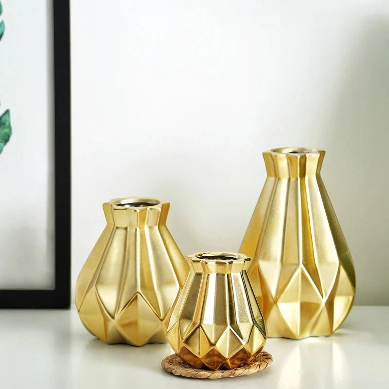 Three Gold Flower Vases on a white  surface next to a picture frame