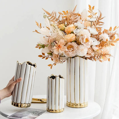 three Gold and White Vases with flowers inside on a white table