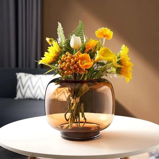 Large Round Vase on a white table with yellow flowers inside with a grey couch in the background