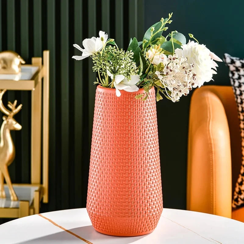 Plastic Cylinder Vase in orange on a white table with flowers inside