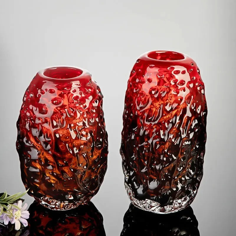 Two Red Glass Vases on a shiny surface next to flowers