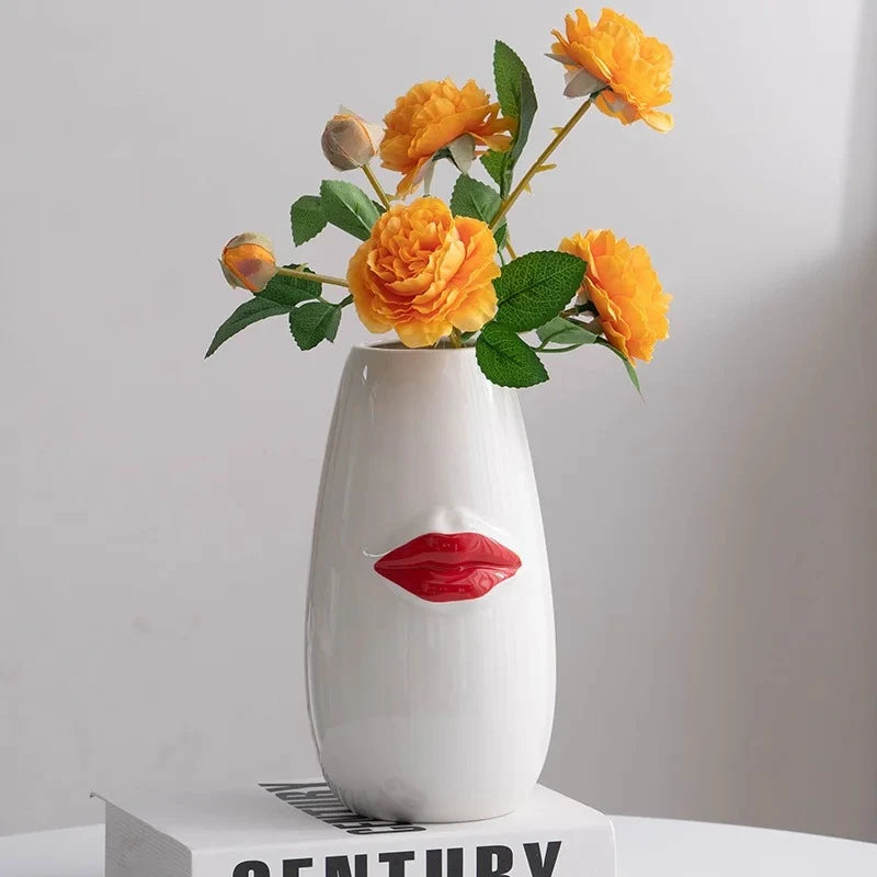 Red and White Vase with orange flowers inside standing on a book