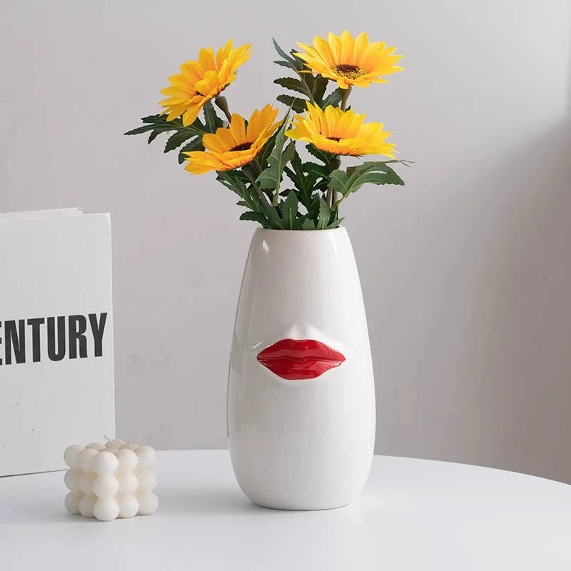 Red and White Vase with yellow flowers inside next to a candle 