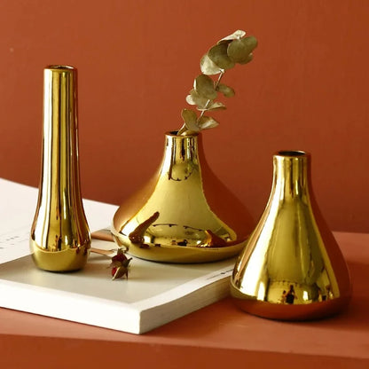 Three Small Gold Vases on an orange surface with dried flowers inside