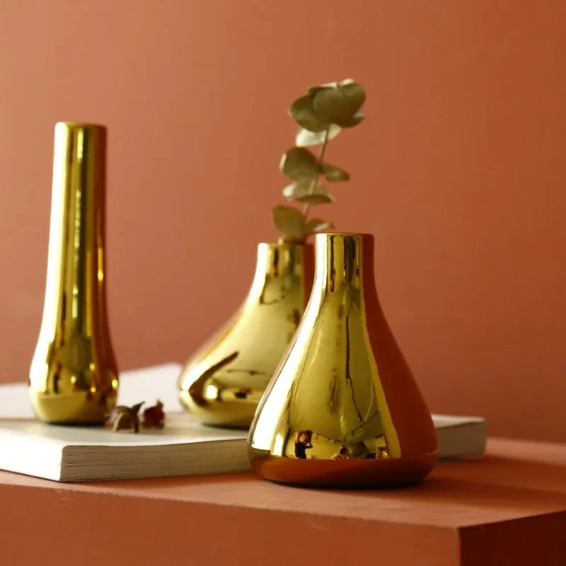 Three Small Gold Vases on an orange surface with dried flowers inside