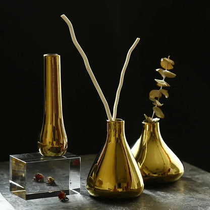 Three Small Gold Vases on a gray surface next to decorational elements