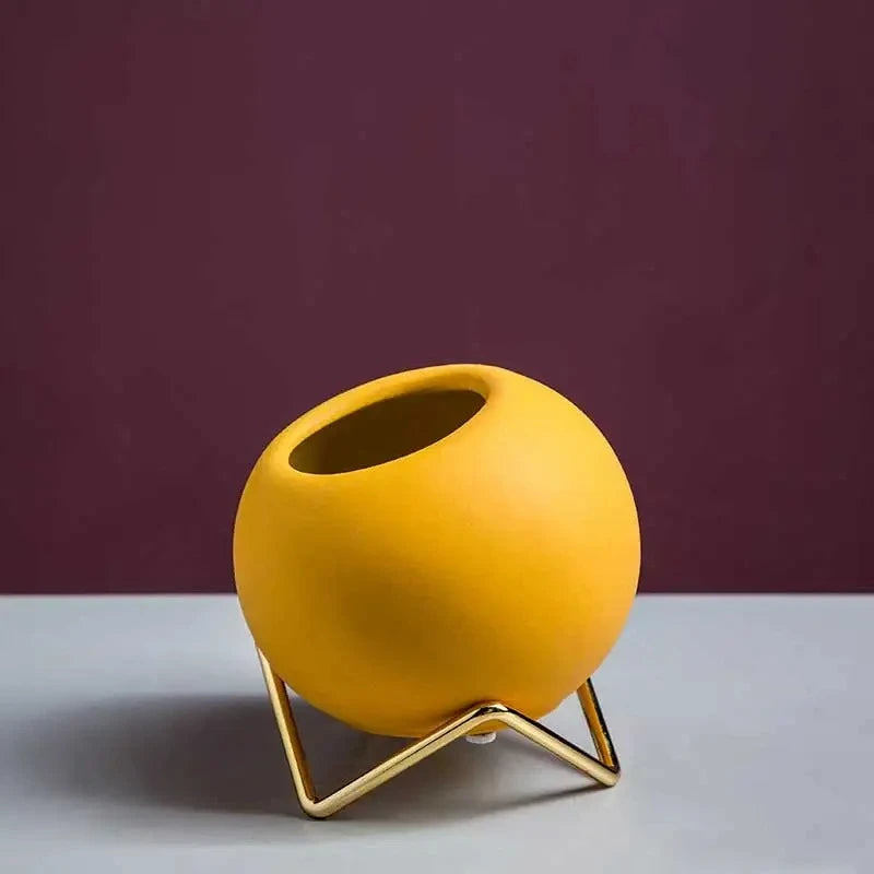 Small Round Vase in yellow in front of a wine red background on a white surface