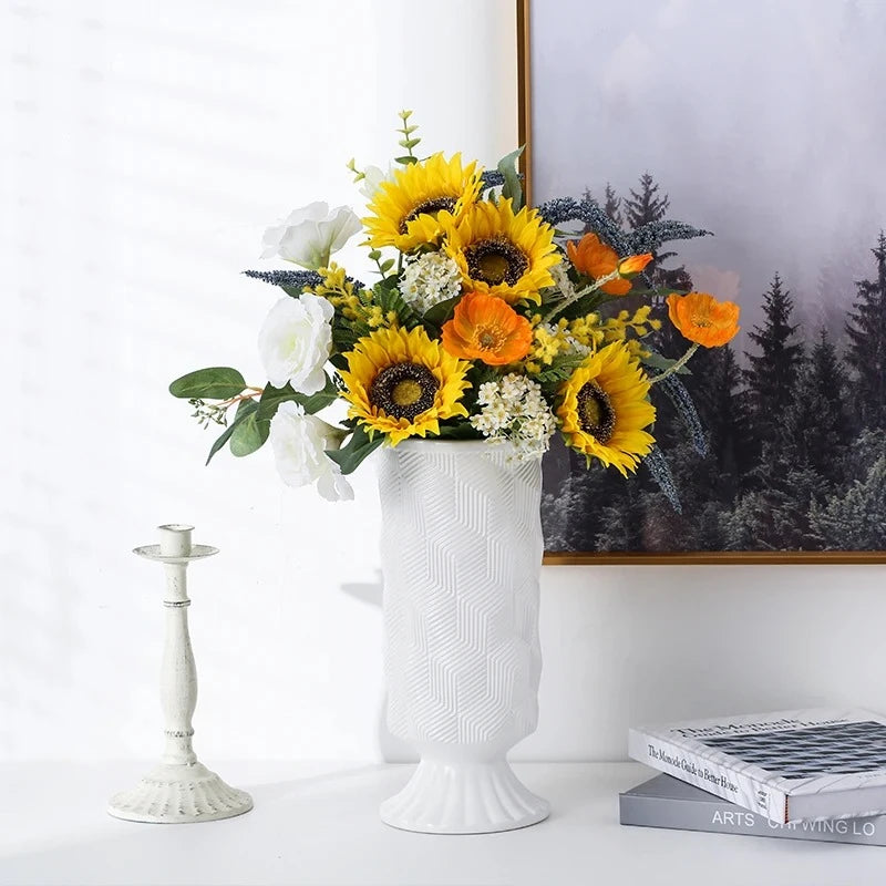 White Cylinder Vase with flowers inside sitting on a shelf with decorative elements next to it