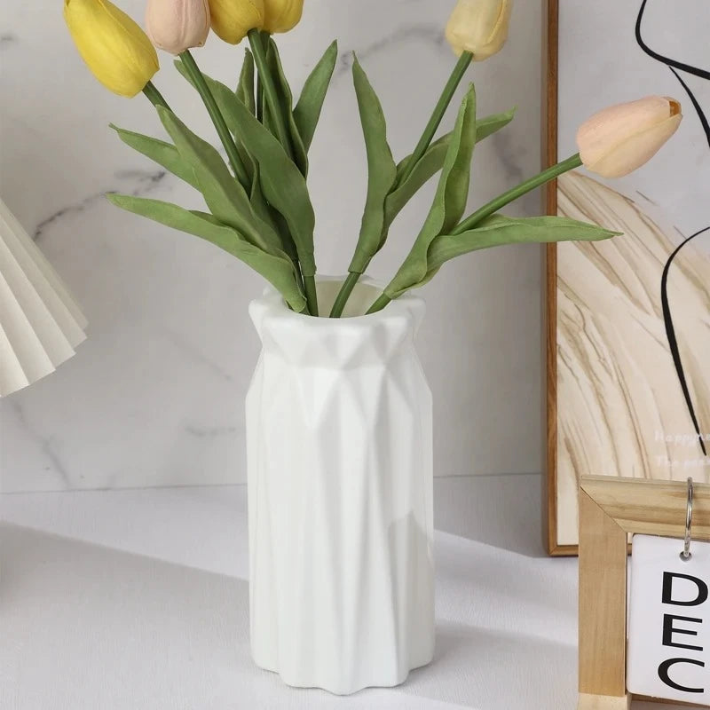 White Plastic Vase with flowers inside on a white surface next to an image frame